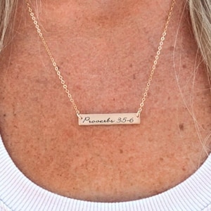Könnte beinhalten: Eine goldene Halskette mit einer dünnen Kette und einem rechteckigen Anhänger, auf dem "Sprüche 3:5-6" in kursivschrift steht.