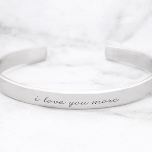 May include: A silver bangle bracelet with the inscription "i love you more".