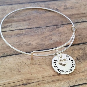 May include: Silver expandable bangle bracelet with a charm featuring a heart and the coordinates 37.245 and 8.104.