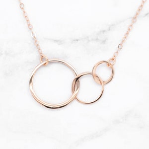May include: A rose gold necklace with three interconnected circles. The circles are of different sizes and are connected to a delicate chain.