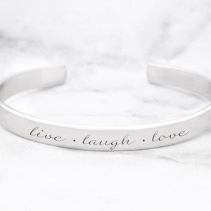 May include: Silver bangle bracelet with the inscription "live. laugh. love."