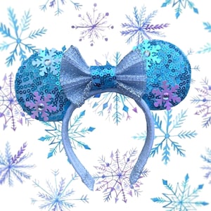 May include: A light blue headband with sequined ears and a matching bow. The ears are decorated with light blue sequins and purple snowflake accents. The background features a pattern of blue and purple snowflakes.