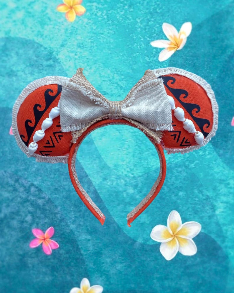 K&ouml;nnte beinhalten: Ein rotes Stirnband mit kreisf&ouml;rmigen Ohrakzenten mit einem Wellenmuster und geometrischen Designs. Die Ohren sind mit wei&szlig;en Muschelakzenten und einer beigen Schleife verziert. Das Stirnband ist mit einer beigen Bord&uuml;re verziert und befindet sich vor einem blauen Hintergrund mit floralen Akzenten.