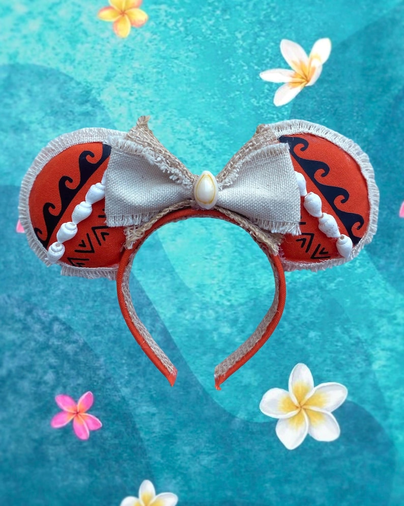 K&ouml;nnte beinhalten: Ein rotes Stirnband mit kreisf&ouml;rmigen Ohrakzenten mit einem Stammesdesign, schwarzen Wellenmustern und wei&szlig;en Muschelschmuck. Eine beige Schleife mit einem Muschelzentrum verziert die Oberseite. Das Stirnband ist von einem blauen Hintergrund mit Blumenakzenten umgeben.
