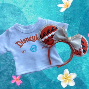 K&ouml;nnte beinhalten: Ein wei&szlig;es T-Shirt mit "Disneyle" in orangefarbener Schrift und einem blauen Wirbellogo, kombiniert mit einem passenden Stirnband. Das Stirnband hat orangefarbene Ohren mit einem Wellenmuster und eine cremefarbene Schleife. Das Stirnband ist rot.