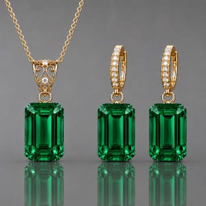 May include: A gold jewelry set consisting of a necklace and two hoop earrings. Each piece features a large, emerald-cut green gemstone. The necklace pendant has an ornate, filigree-style gold bail, while the hoop earrings are lined with small, clear, round-cut stones.