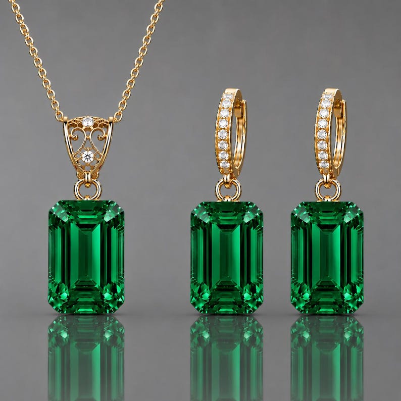 May include: A gold jewelry set consisting of a necklace and two hoop earrings. Each piece features a large, emerald-cut green gemstone. The necklace pendant has an ornate, filigree-style gold bail, while the hoop earrings are lined with small, clear, round-cut stones.
