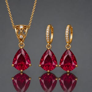Könnte beinhalten: Ein goldfarbenes Schmuckset bestehend aus einer Halskette und einem Paar Creolen. Jedes Stück verfügt über einen großen, birnenförmigen, tiefroten Edelsteinanhänger. Die Kettenöse und die Creolen sind mit kleinen, klaren, funkelnden Steinen besetzt.