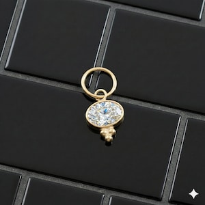 May include: A gold pendant with a large, oval-cut diamond. The diamond is set in a gold bezel and has a brilliant sparkle. The pendant has a small, decorative gold element at the bottom and a loop at the top for a chain.