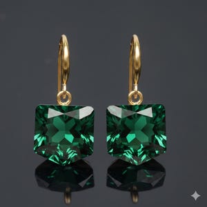 Op de afbeelding: Een paar goudkleurige oorbellen met grote, vierkant geslepen, smaragdgroene edelstenen. De edelstenen zijn gefacetteerd, waardoor een sprankelend effect ontstaat. De oorbellen hebben een eenvoudig, elegant ontwerp met een haaksluiting.