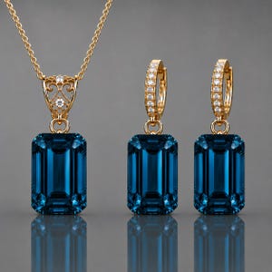 May include: A gold jewelry set consisting of a pendant necklace and two matching hoop earrings. Each piece features a large, emerald-cut, deep blue gemstone suspended from a gold setting adorned with small, clear, sparkling accent stones.