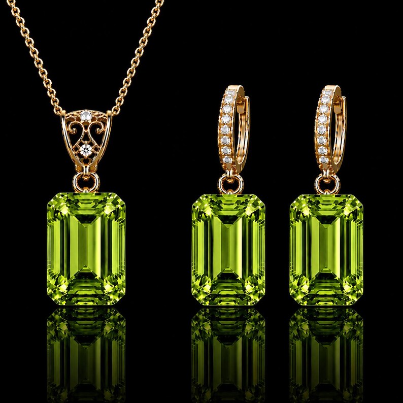 May include: A jewelry set consisting of a necklace and two hoop earrings crafted from gold-toned metal. Each piece features a large, rectangular, emerald-cut lime green gemstone. The necklace bail and earring hoops are accented with small, clear, round stones.