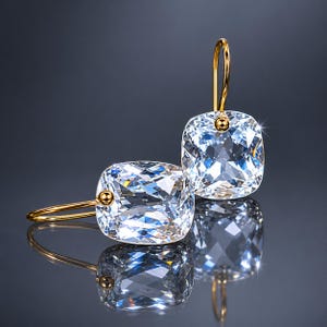 May include: A pair of gold-tone drop earrings featuring large, clear, cushion-cut faceted stones. Each earring is suspended from a simple gold-tone hook, with a small gold-tone bead accent connecting the hook to the square-shaped crystal stone.