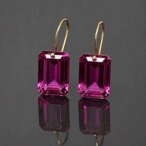 May include: A pair of drop earrings featuring large, rectangular, faceted magenta gemstones. Each stone is suspended from a thin, curved gold-tone wire hook that attaches to the top centre of the gemstone with a small, round gold-tone bead detail.