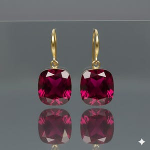 Puede incluir: Un par de pendientes colgantes dorados con grandes piedras preciosas rojas cuadradas. Las piedras están facetadas, captando la luz. Diseño simple y elegante, ideal para ocasiones especiales.