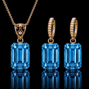 May include: A jewelry set consisting of a necklace and two hoop earrings, each featuring a large, rectangular, emerald-cut blue gemstone. The gold-toned settings are accented with small, clear, round-cut stones on the pendant bail and hoops.