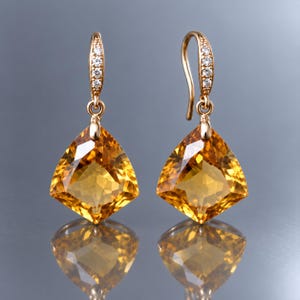 Peut inclure: Une paire de boucles d'oreilles pendantes en or avec de grandes pierres précieuses citrines jaunes de forme triangulaire à facettes. Les crochets incurvés sont ornés de petits diamants blancs ronds, créant un bijou brillant et réfléchissant.