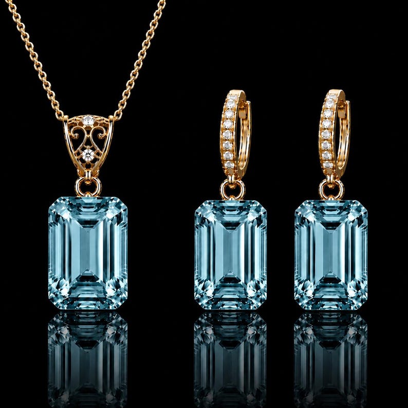 May include: A jewelry set consisting of a necklace and two hoop earrings in gold. Each piece features a large, rectangular, light blue gemstone. The necklace pendant and earring hoops are accented with small, clear, round-cut white stones.
