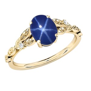 Puede incluir: Un anillo de oro con una piedra preciosa ovalada de color azul oscuro con un patrón en forma de estrella. La banda del anillo y los elementos decorativos, incluyendo diseños en forma de hojas y pequeños diamantes, son de un tono dorado cálido, creando un aspecto elegante.