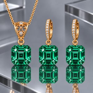 Op de afbeelding: Een gouden sieradenset bestaande uit een ketting met hanger en twee bijpassende oorringen. Elk sieraad is voorzien van een grote, vierkant geslepen smaragdgroene edelsteen. De hanger en de oorringen zijn bezet met kleine, heldere steentjes.