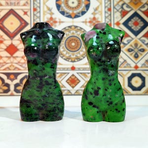 May include: Two green and black gemstone torso sculptures. The sculptures are polished and have a smooth surface. The sculptures are in the shape of a female torso.