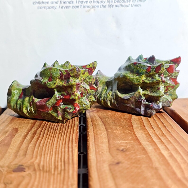 May include: Two dragon head sculptures. The sculptures are green with red accents and are made of stone. The dragon heads are resting on a wooden surface. The text in the background says, "children and friends. I have a happy life because of their company. I even can't imagine the life without them."
