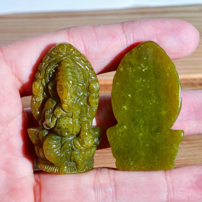 Puede incluir: Dos tallas de jade verde del dios hind&uacute; Ganesha. Una es una escultura tridimensional detallada, la otra una pieza plana y lisa de forma ovalada. Las tallas se sostienen en una mano.