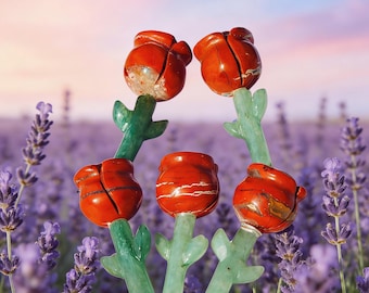 May include: Six handcrafted stone rose sculptures. The rose blossoms are a vibrant red-orange color, with green stems and leaves. The background is a lavender field under a pink and blue sky. These decorative sculptures are ideal for home decor.