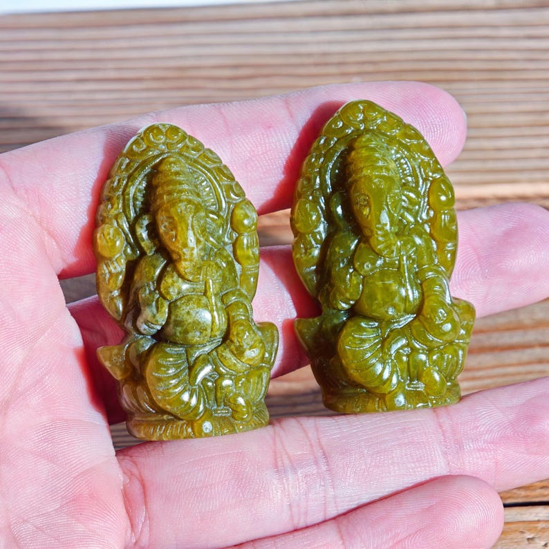 Puede incluir: Dos estatuas de Ganesh de color jade. Las estatuas est&aacute;n talladas con detalles intrincados, que representan a la deidad hind&uacute; en posici&oacute;n sentada. Las estatuas son de color verde vibrante y se sostienen en la mano de una persona.