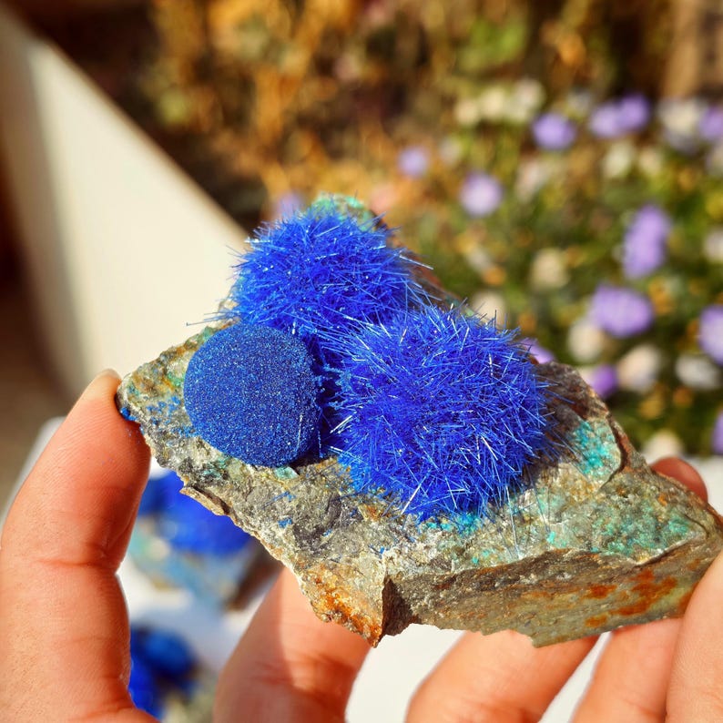 Puede incluir: Primer plano de una formaci&oacute;n rocosa con vibrantes grupos de minerales azules. La roca tiene una superficie rugosa y texturizada con parches verdes y azules. Las formaciones minerales azules son esf&eacute;ricas y puntiagudas.