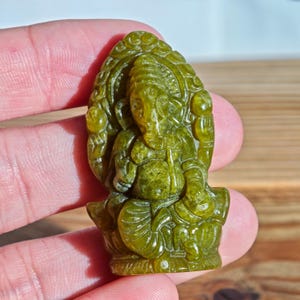 Puede incluir: Una figura tallada en piedra preciosa verde del dios hind&uacute; Ganesha. La escultura representa a Ganesha sentado, con intrincados detalles en su forma y los elementos decorativos circundantes. La figura mide aproximadamente 5 cm de altura.