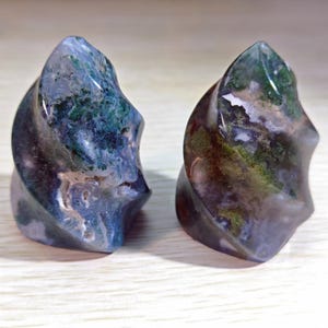 May include: Two polished, abstract stone sculptures. The stones feature a swirling design in shades of blue, green, and brown. The sculptures have a smooth, glossy finish and are displayed side by side.