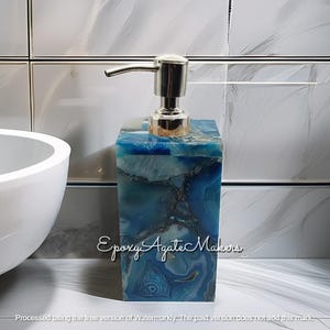 May include: A blue and white agate soap dispenser with a silver pump. The dispenser is rectangular and features a unique, marbled pattern. The text "Epoxy Agate Makers" is visible on the front.
