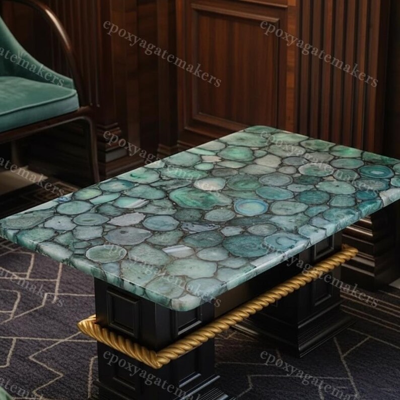 Op de afbeelding: Een rechthoekige salontafel met een moza&iuml;ekblad van groene en blauwe agaat schijfjes. De tafel heeft een zwart onderstel met gouden touwachtige accenten. De tafel is een uniek meubelstuk.