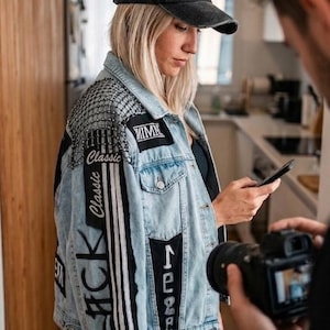 Puede incluir: Chaqueta vaquera de lavado claro con parches y texto que dice "Classic" y "1988". La chaqueta tiene un detalle de hombro con tachuelas negras y plateadas y se usa con una gorra negra.