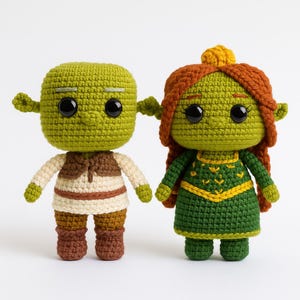 Puede incluir: Dos muñecos de ganchillo hechos a mano, uno verde con chaleco marrón y el otro verde con pelo rojo y vestido verde. Los muñecos tienen grandes ojos negros y están uno al lado del otro. Los muñecos son una representación caprichosa de una película de animación popular.