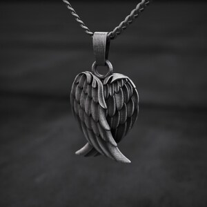 May include: A silver-toned pendant featuring a detailed angel wing design. The pendant is suspended from a matching chain, creating a monochromatic aesthetic. The wings are intricately crafted, showcasing individual feather details. The background is blurred, emphasizing the pendant's form.