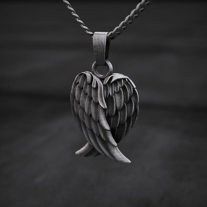 May include: A silver-toned pendant featuring a detailed angel wing design. The pendant is suspended from a matching chain, creating a monochromatic aesthetic. The wings are intricately crafted, showcasing individual feather details. The background is blurred, emphasizing the pendant's form.
