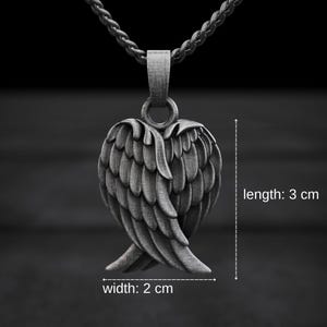 May include: A silver-colored pendant necklace featuring a detailed wing design. The pendant measures 3 cm in length and 2 cm in width. The necklace has a dark background.