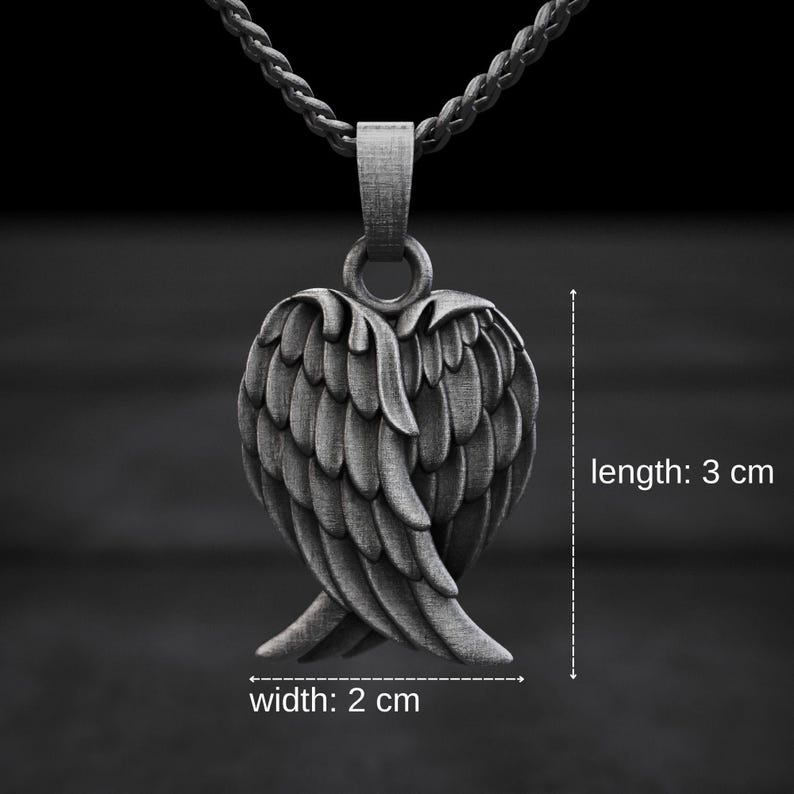 May include: A silver-colored pendant necklace featuring a detailed wing design. The pendant measures 3 cm in length and 2 cm in width. The necklace has a dark background.