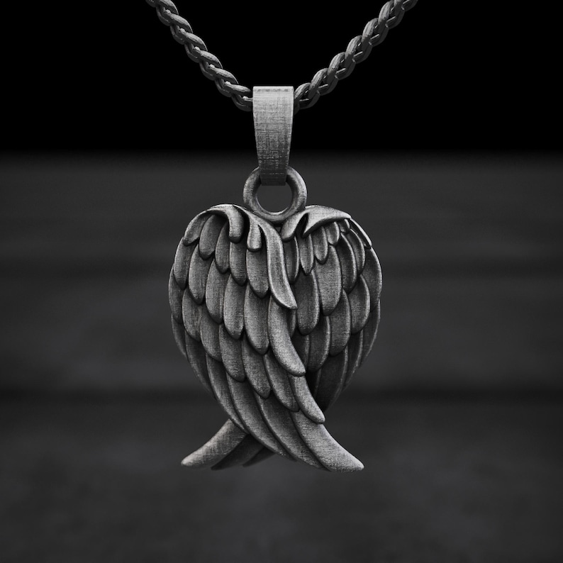 May include: A silver-colored pendant necklace featuring a detailed wing design. The pendant is suspended from a matching chain, with the wings' feathers meticulously rendered. The necklace is set against a dark background.