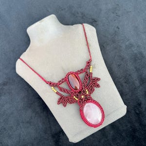 Può includere: Collana in macramè fatta a mano, color bordeaux. Presenta un grande pendente ovale in quarzo rosa e una pietra ovale marrone più piccola. Il design include nodi intricati e piccole perline dorate.