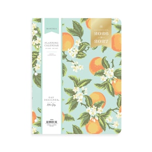 May include: A monthly planning calendar by Day Designer for 2026 to 2027. The cover features a light blue background with a pattern of orange fruit, green leaves, and white blossoms. A vertical white band on the left displays text and a barcode.