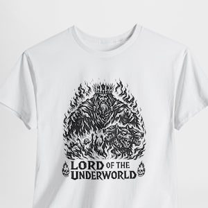 May include: White t-shirt featuring a black graphic of a crowned figure surrounded by flames and two snarling beasts. The text "LORD OF THE UNDERWORLD" is printed below the graphic, with skull accents.