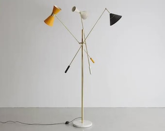 Può includere: Lampada da terra multicolore con tre paralumi regolabili. I paralumi sono gialli, bianchi e neri, e la lampada ha un palo dorato e una base in marmo bianco. Il design della lampada è moderno.