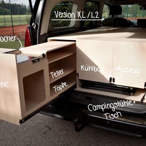 Peut inclure: Un kit d'aménagement intérieur en bois clair pour fourgon aménagé installé à l'arrière d'un véhicule. Il comprend une cuisine coulissante avec des sections étiquetées pour un réchaud, des assiettes, des casseroles, une glacière et du rangement.