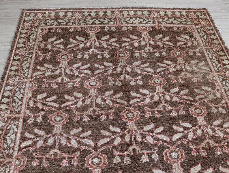 May include: A rectangular area rug featuring a dark brown background with a repeating floral and vine pattern in shades of cream and muted pink. The design includes stylized flowers and leaves arranged in a grid, framed by a decorative border.
