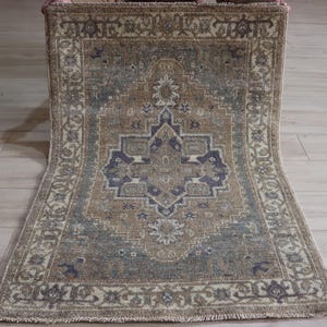 May include: A rectangular rug with a central medallion design. The rug features a colour palette of brown, blue, and cream. The border has a detailed floral pattern. The rug is made of a woven material and has a distressed, vintage look.
