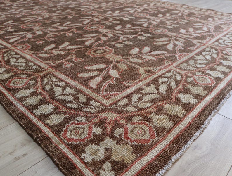 May include: A rectangular area rug featuring a deep brown background with a repeating floral and vine pattern in cream and muted coral tones. The design includes a prominent border with stylized blossoms and leaves framing the central field.