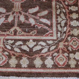 May include: A rectangular area rug featuring a deep brown background with a repeating floral and leaf pattern in shades of cream and muted coral. The design includes a wide border with stylized blossoms and foliage, finished with a short fringe.